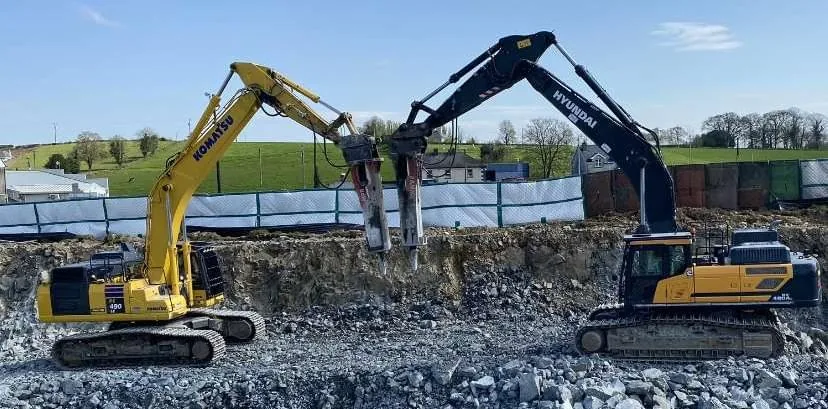 Two excavators with hydraulic breakers working side by side in a rocky pit