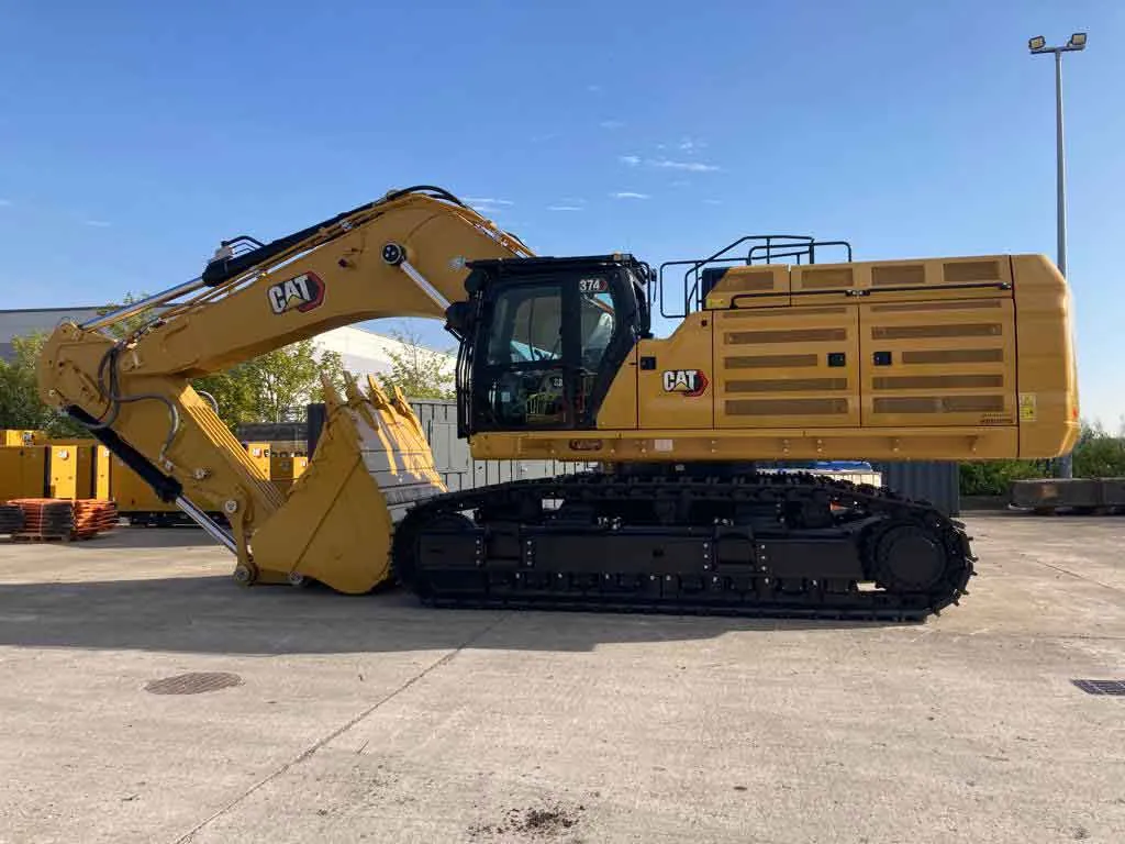 Side profile of a yellow Caterpillar excavator parked in a staging yard
