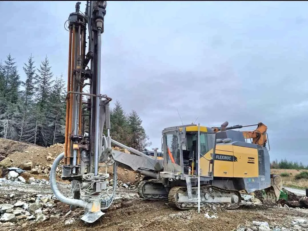 Tracked blasthole drilling rig standing on a rocky site near forestry