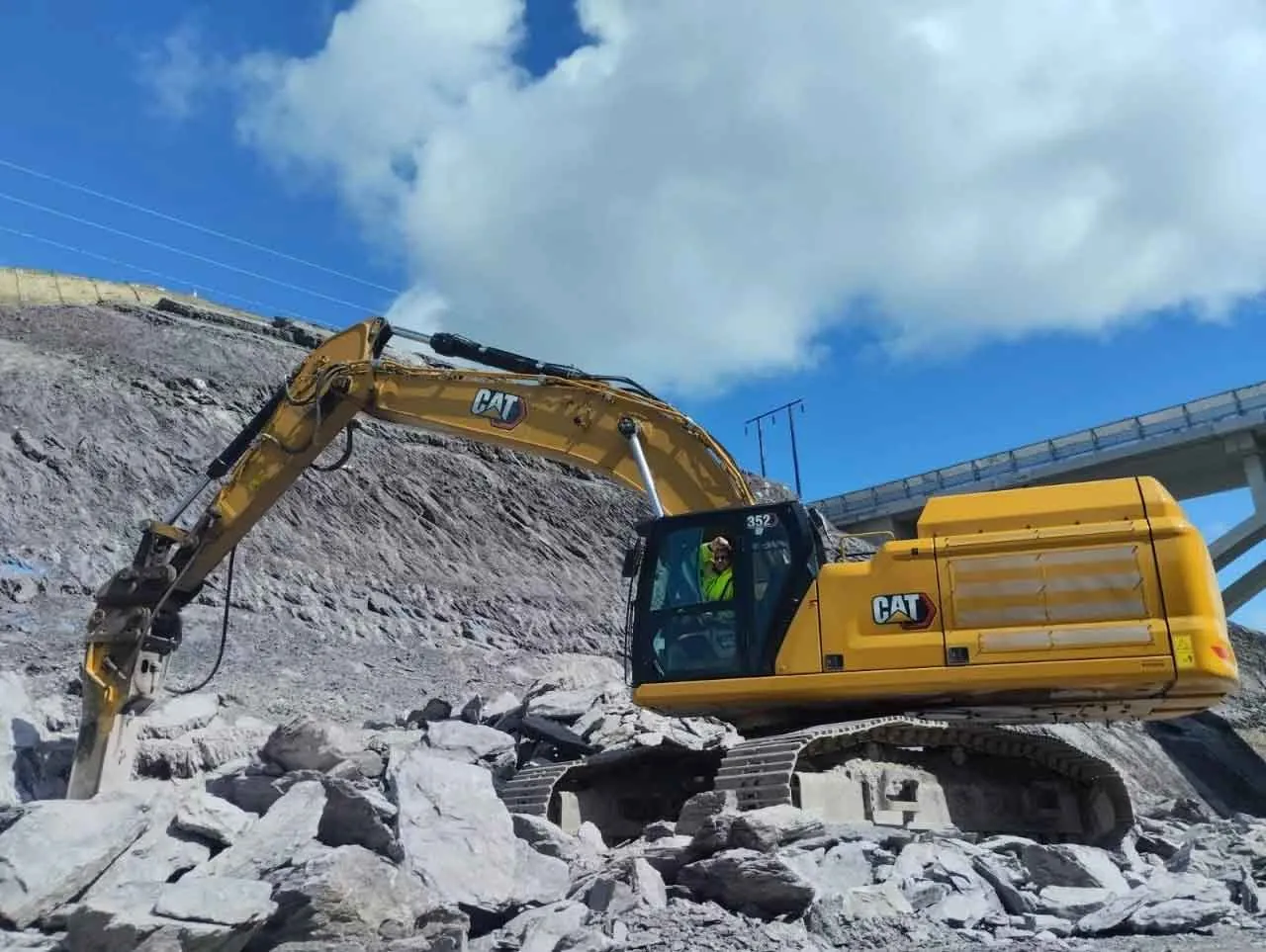 Excavator with a hydraulic breaker working rock near a concrete bridge on a road scheme